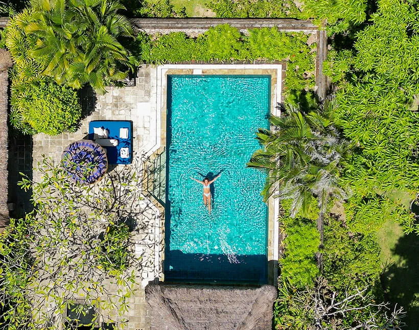 Woman swimming in resort pool surrounded by lush greenery The Oberoi Bali